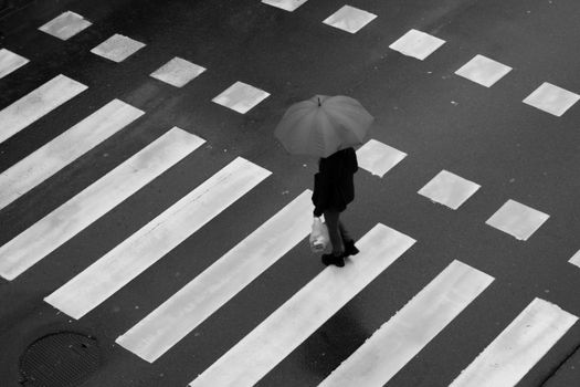 Man walking across wet city crosswalk holding an umbrella.