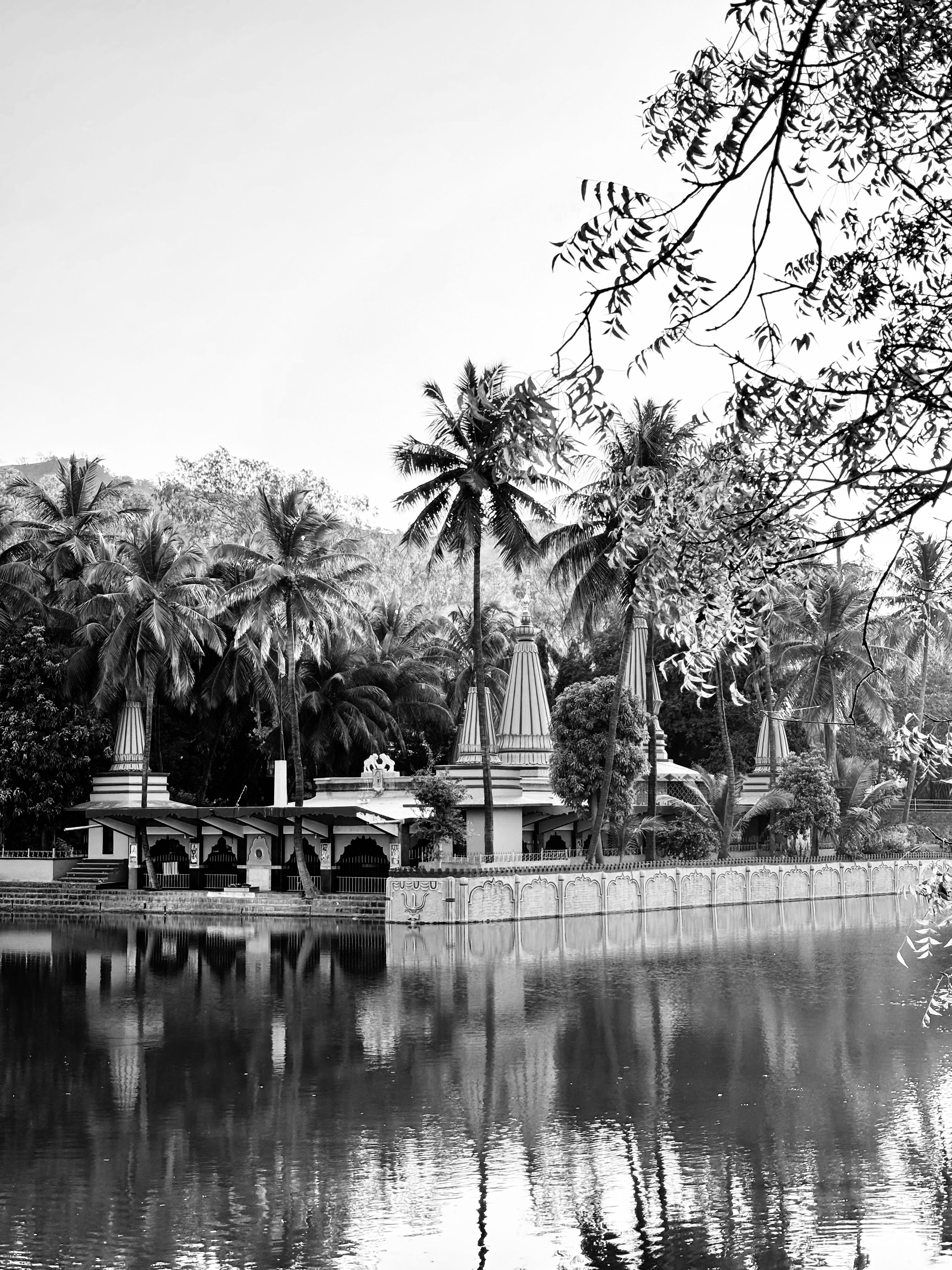 Black and white photo of Ramdara Temple in Pune with reflections in a serene lake surrounded by lush trees.
