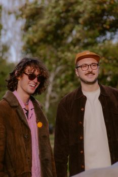 Two friends in casual attire enjoying a sunny day outdoors, smiling and wearing sunglasses.