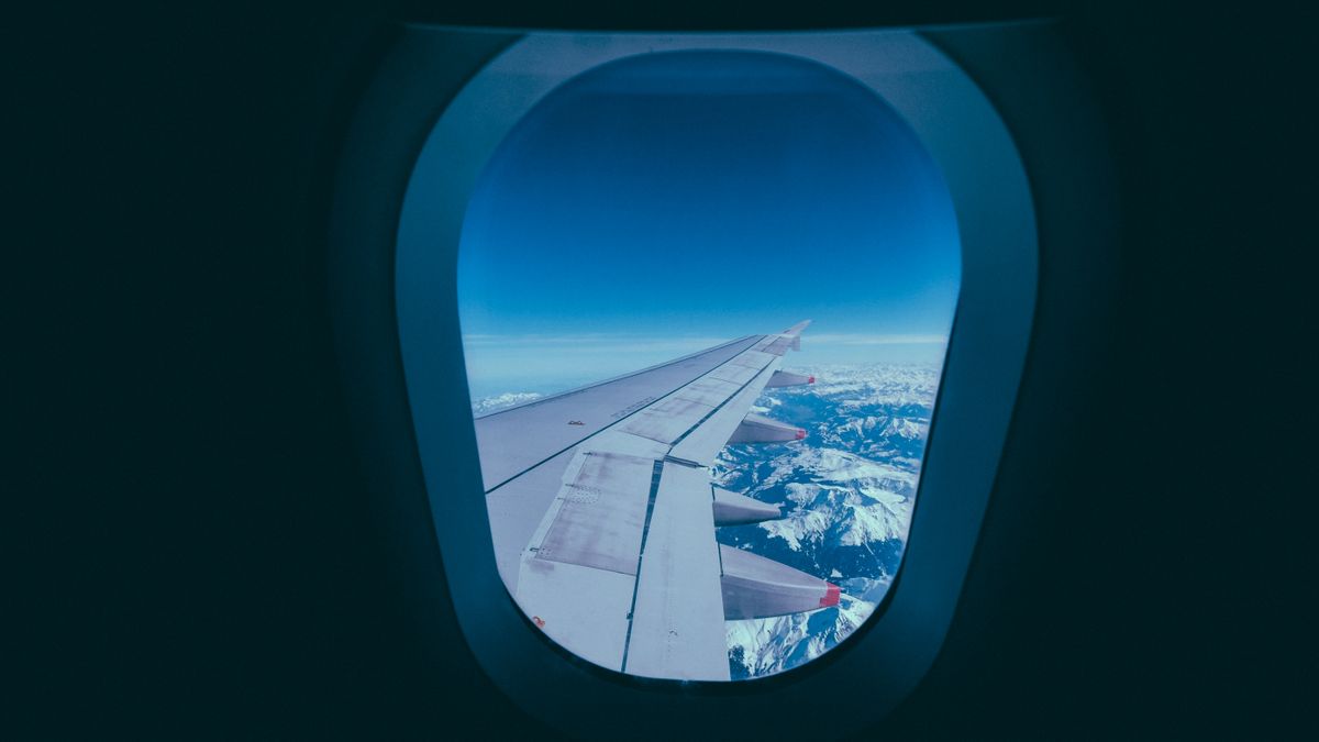 View of an airplane wing and snowy mountains through a window, ideal for travel themes.