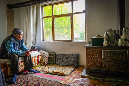 Free An elderly man sits inside by a window, reflecting in a cozy, warm room. Stock Photo