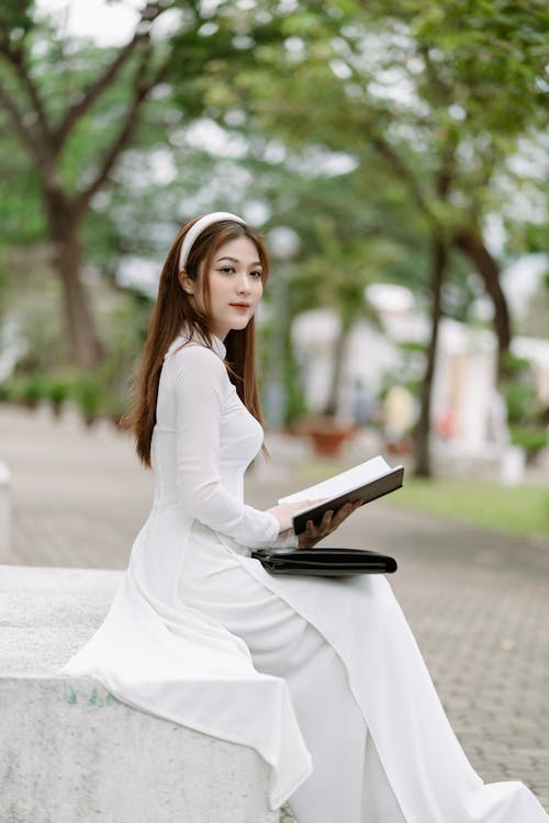 Woman in White Dress Sitting with Book in Park