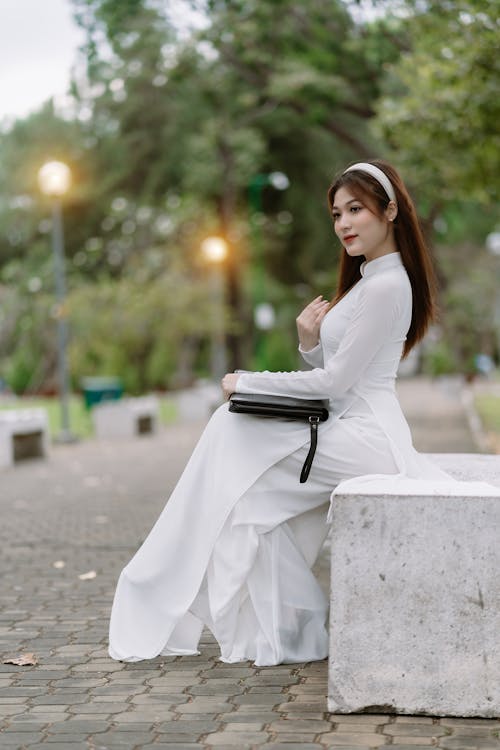 Woman in White Dress Sitting on Wall in Park