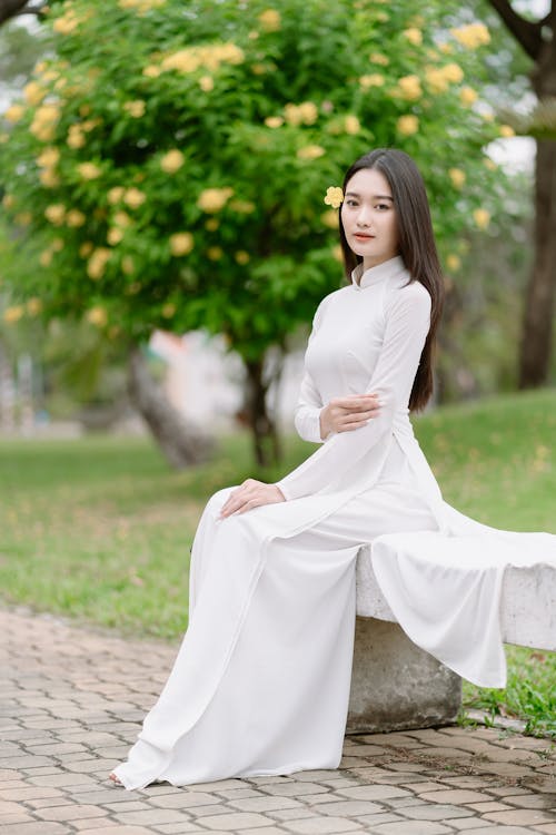 Young Model in a Long White Ao Dai Tunic Sitting on a Park Bench