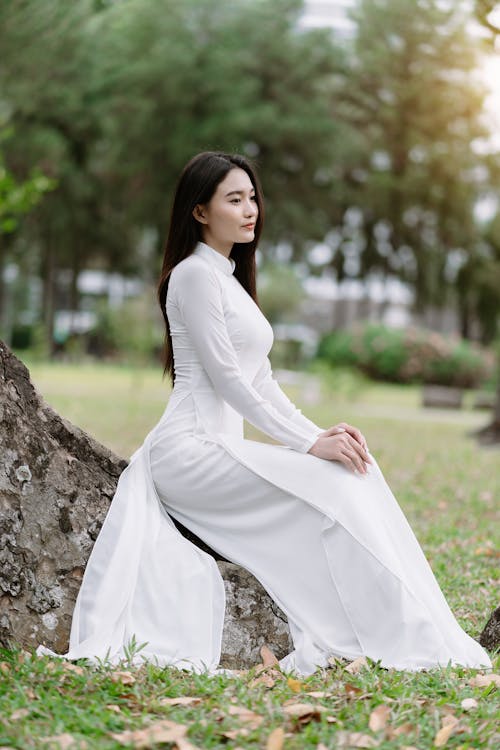 Young Model in Elegant White Ao Dai Tunic Sitting Under a Tree in the Park