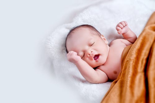 Kostenlos Baby, Das Auf Weißem Fell Mit Brauner Decke Liegt Stock-Foto