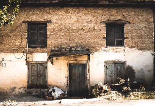 Free A rustic abandoned stone house's facade with old wooden shutters and cracked walls. Stock Photo