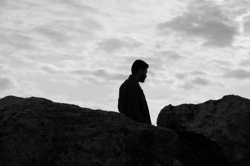 Free Black and white silhouette of a man standing amidst large eroded rocks under a cloudy sky. Stock Photo