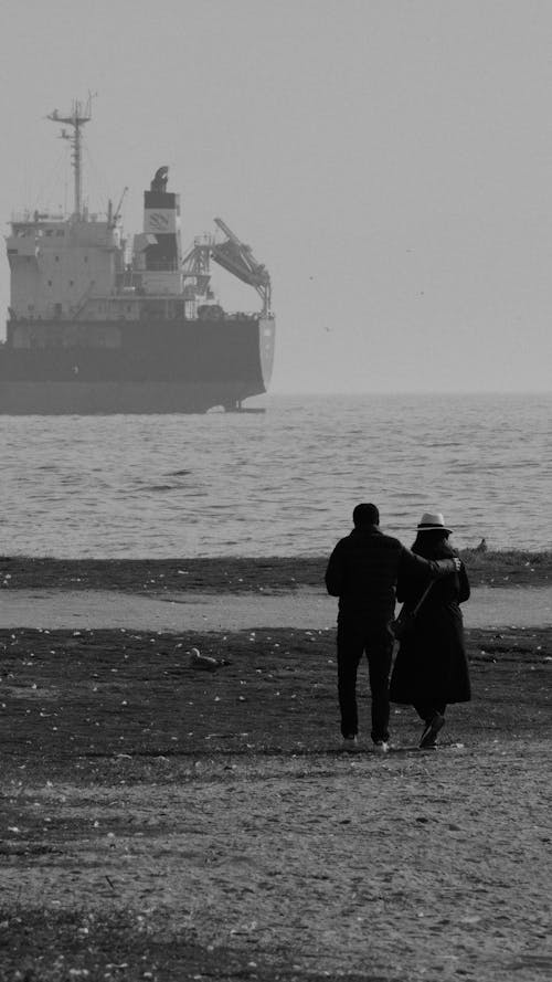 Couple Walking on the Beach where a Cargo Ship Anchored