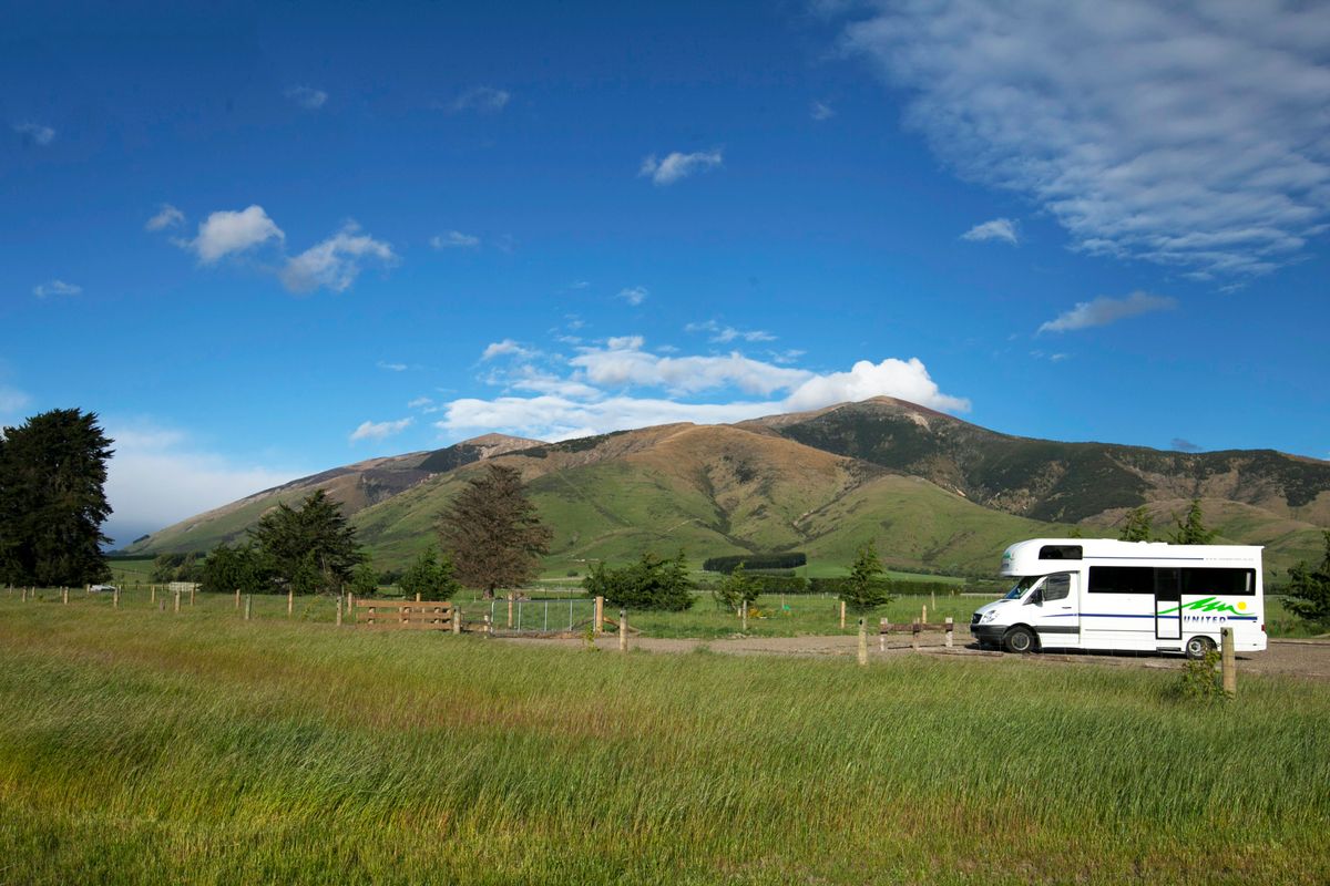 The RV parked in a grassy campsite with mountains behind, finally still after weeks of driving.