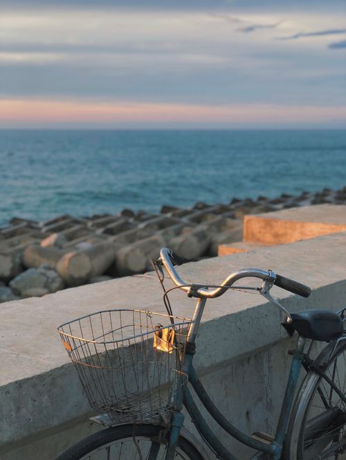 Free A vintage bicycle parked by a seaside wall with a serene ocean sunset backdrop. Stock Photo