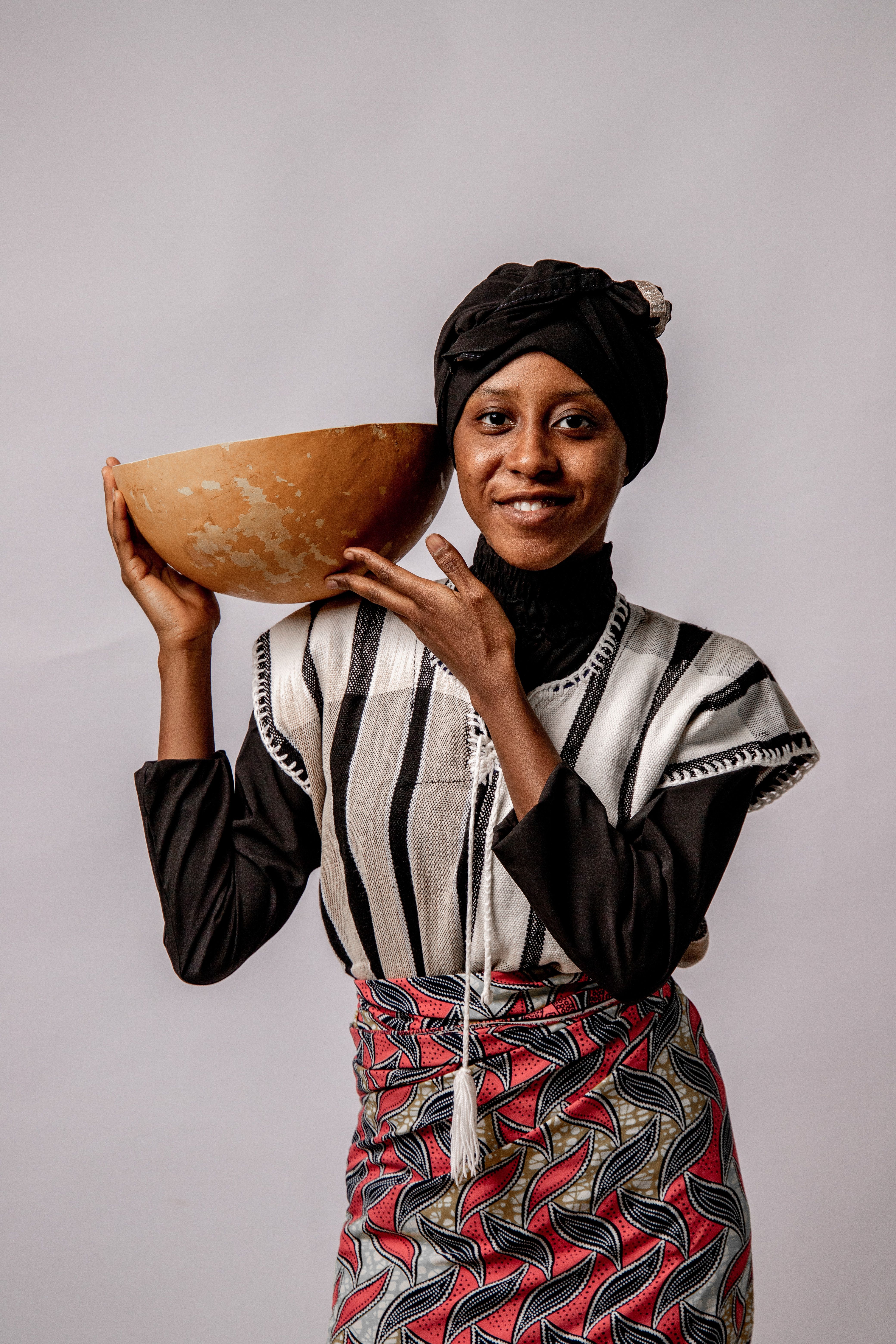 African woman in traditional attire posing with a handcrafted bowl in studio.