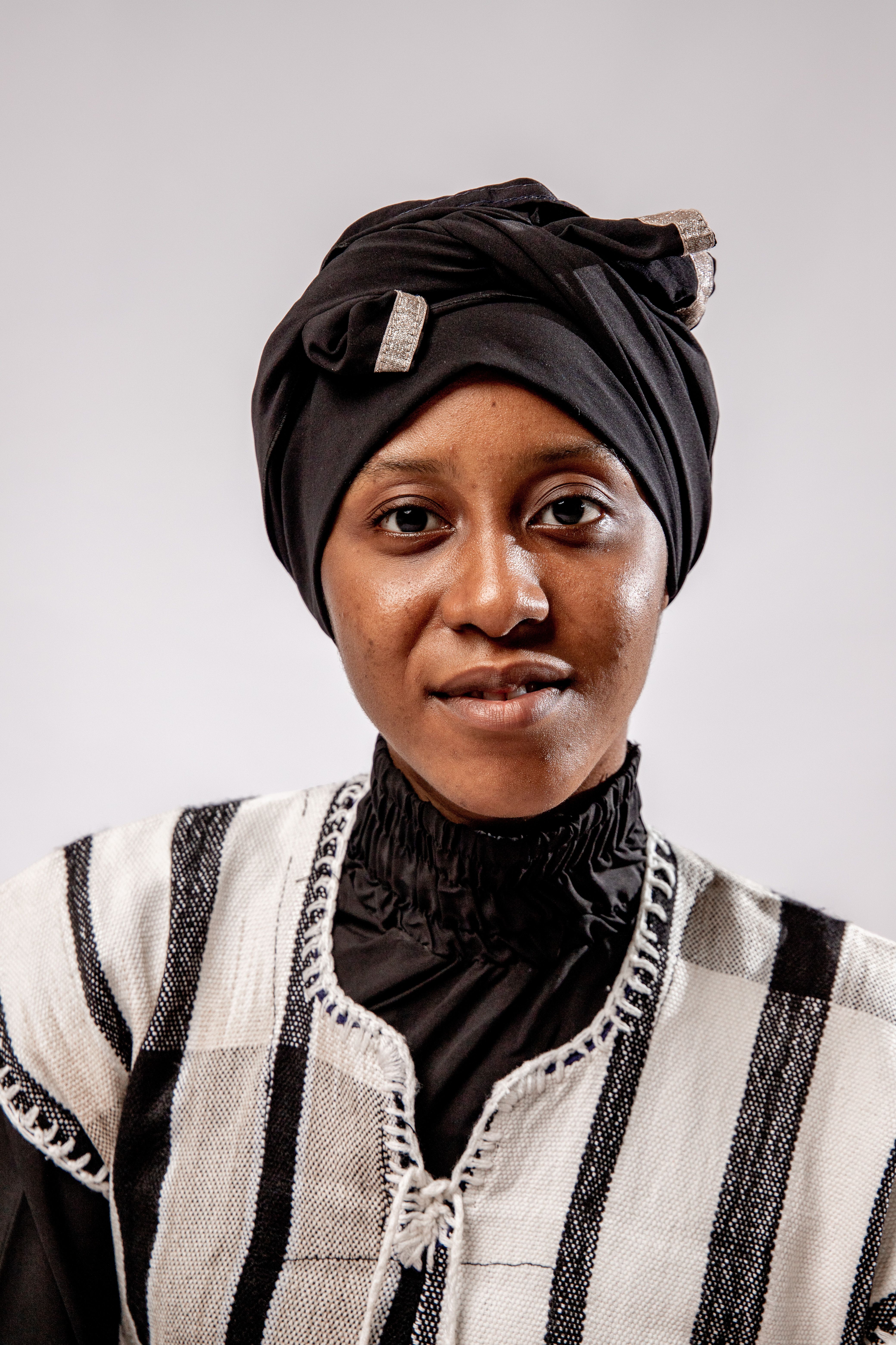 Portrait of an African woman wearing traditional clothing and turban, smiling in a studio setting.