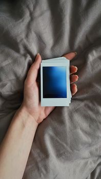 A close-up of a hand holding a stack of blank Polaroid photos on a textured surface.