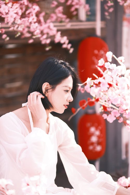 Side View of a Young Woman in a Dress Sitting among Cherry Blossom Branches 