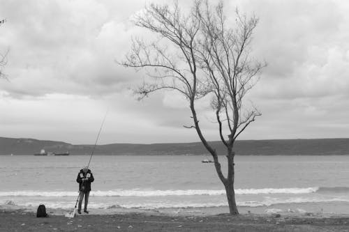 Black and White Photo of a Man Fishing on the Shore 