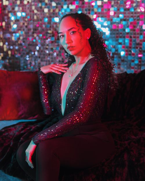 Free Stylish photo of a woman sitting on a couch in shimmering outfit against a colorful background. Stock Photo