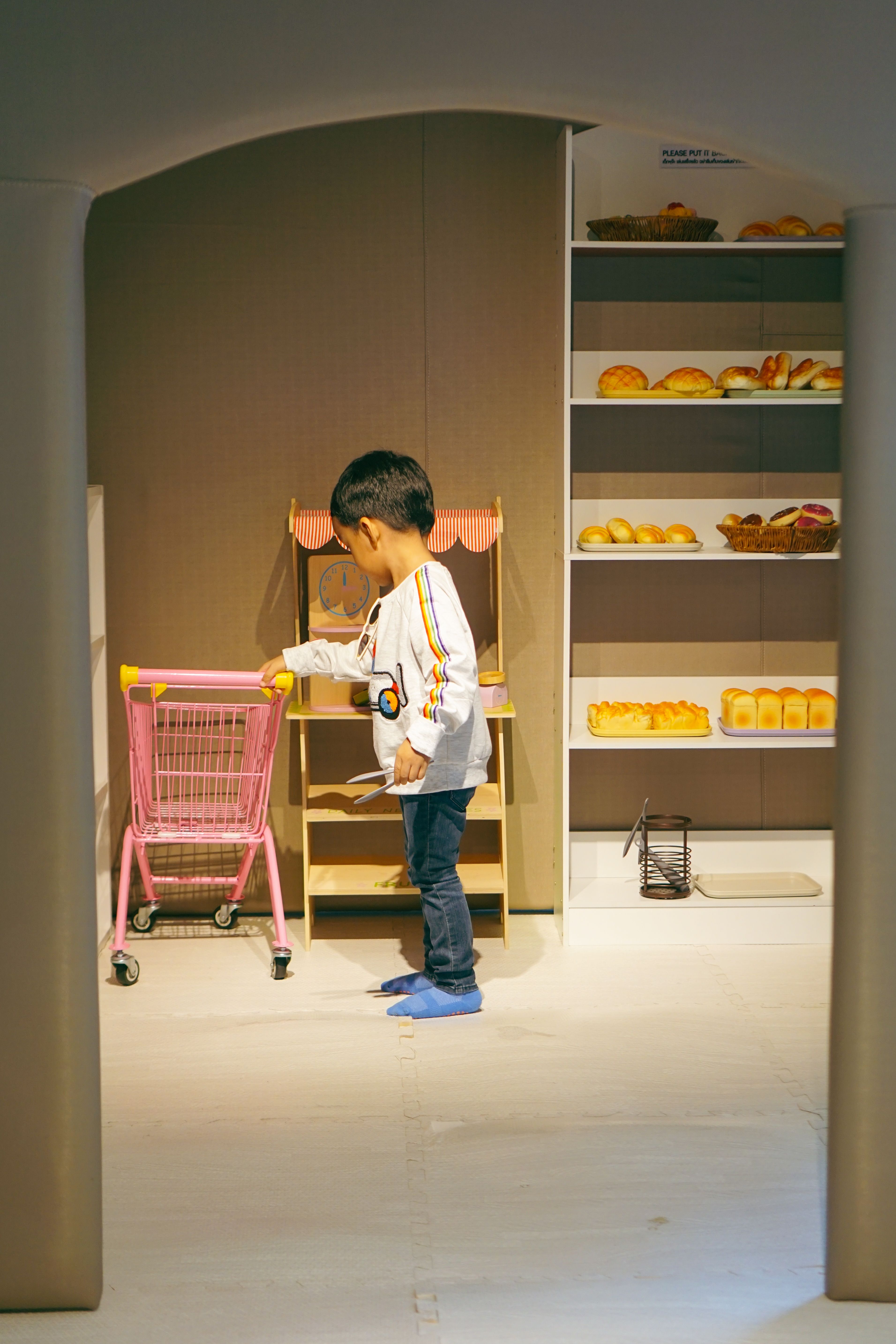 Child pushing a toy shopping trolley in a miniature supermarket play set