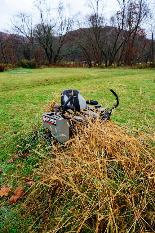 A Lawn Mower Standing on a Field next to a Pile of Straw 