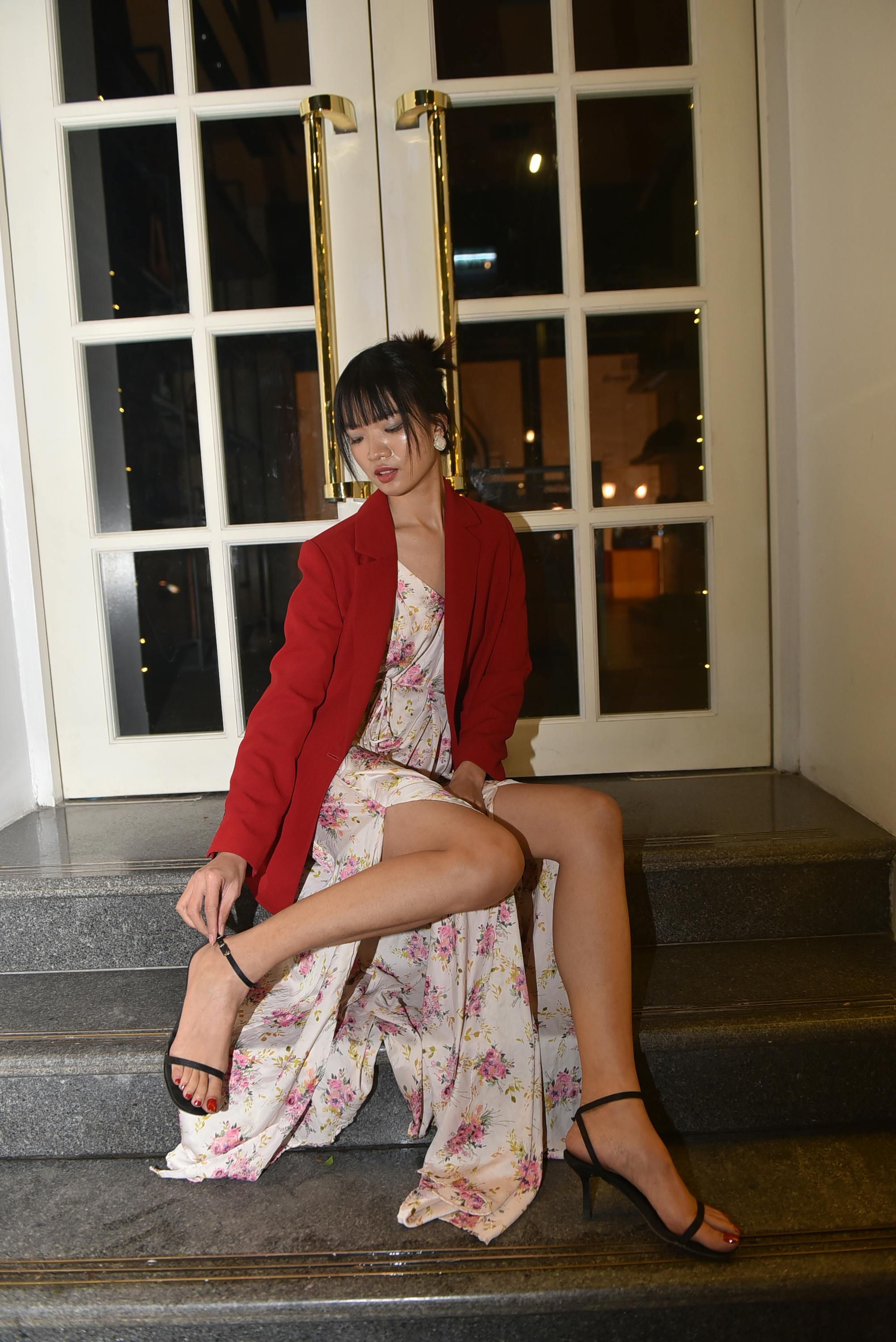 Young woman in floral dress and red jacket sitting on stairs by doors at night.