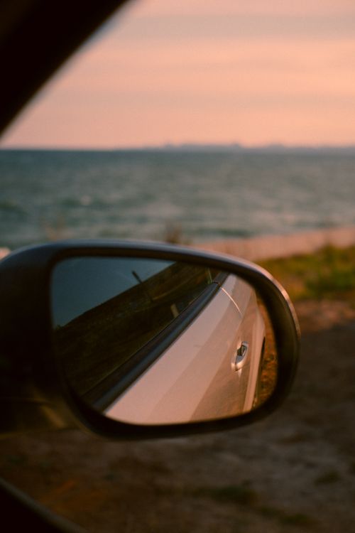 Free View of the ocean through a car's side mirror at sunset. Perfect for travel themes. Stock Photo