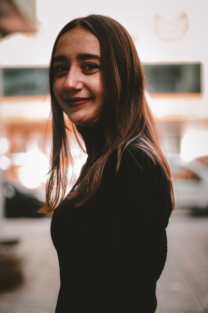 Portrait of a woman smiling in a black turtleneck, captured outdoors with a soft, warm tone.
