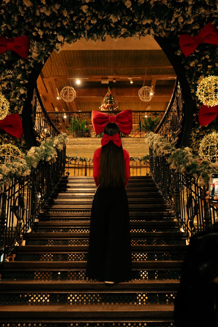 Back View Of An Elegant Woman Standing On The Stairs In A Room With Christmas Decorations