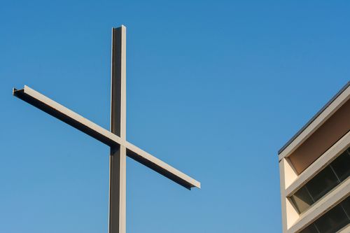 Free A minimalist cross beside a modern building against a clear blue sky, symbolizing simplicity and spirituality. Stock Photo