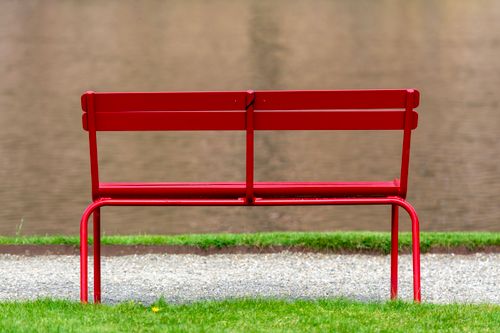 Free A solitary red bench sits by a peaceful riverbank, offering a tranquil spot for relaxation. Stock Photo