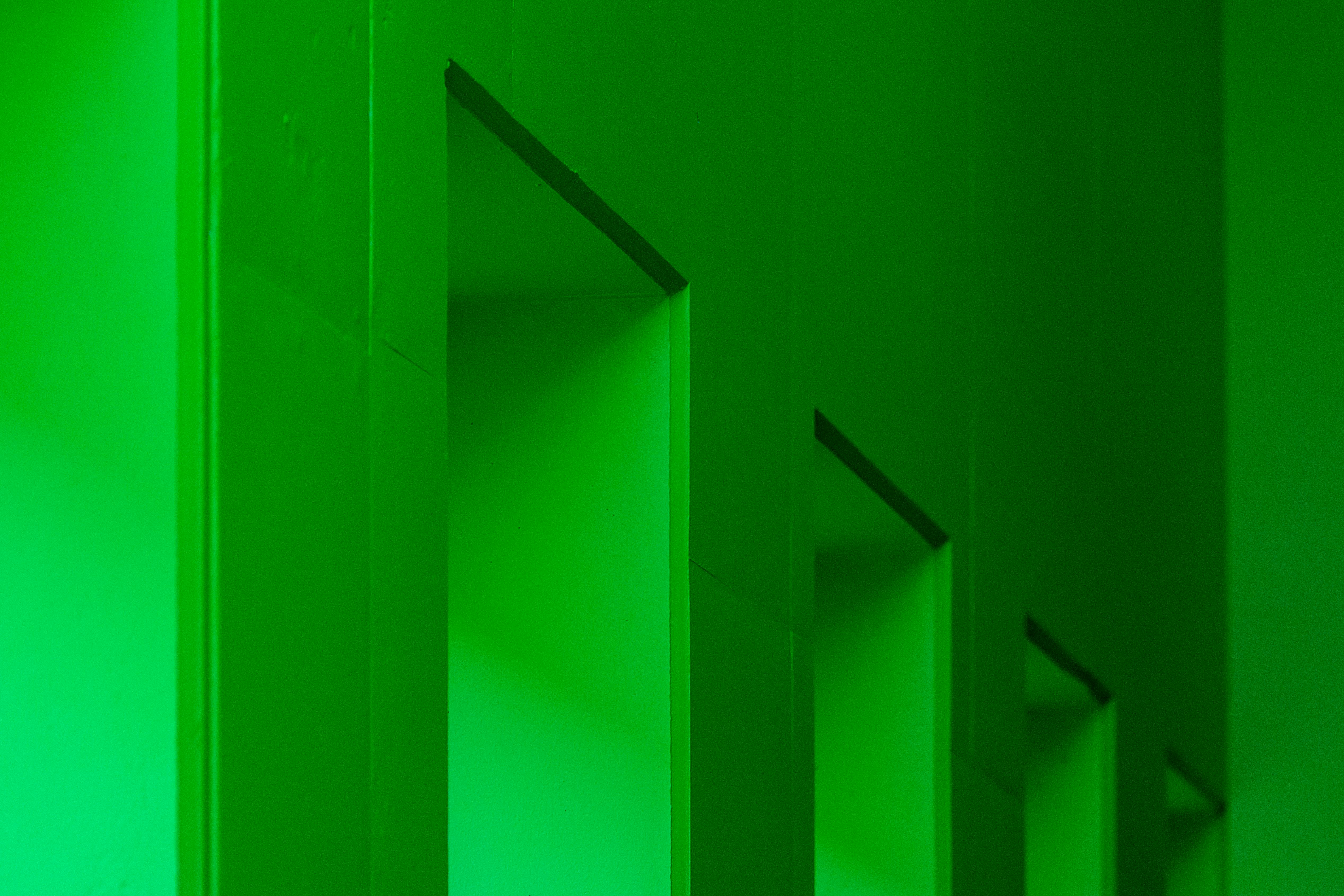 A monochrome geometric pattern of green walls and shadows creates a modern interior design aesthetic.