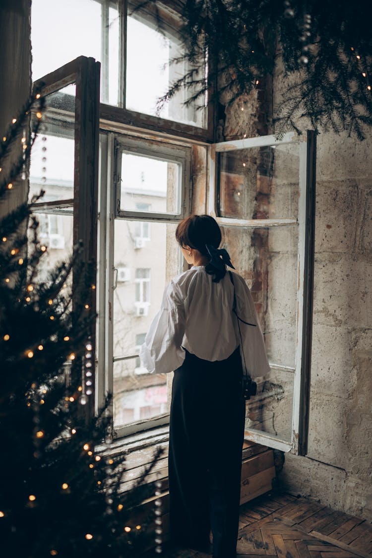 Woman Looking Out The Shabby Window Of A Ruined Room Decorated For The Christmas