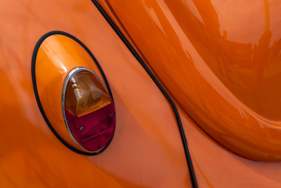 Detailed shot of the taillight on an orange vintage Volkswagen Beetle, showcasing its classic design.