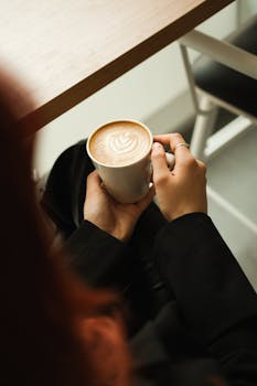 Enjoying a beautifully crafted latte with art, held warmly in a cozy cafe setting.