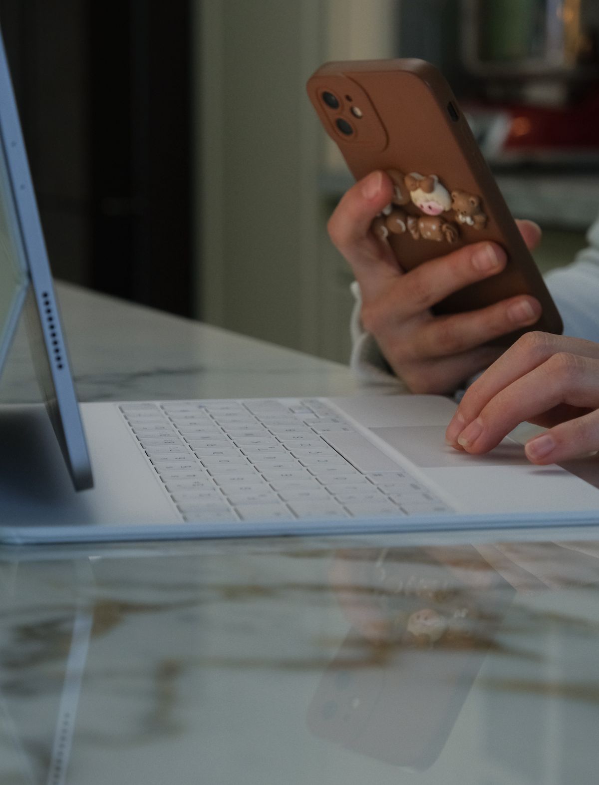 Close-up of hands using a smartphone beside a tablet and keyboard