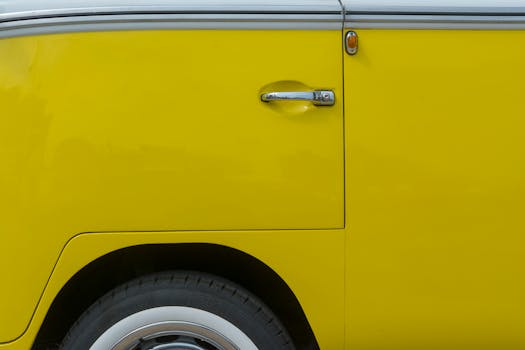 Vibrant yellow Volkswagen van door detail with chrome handle in outdoor setting.