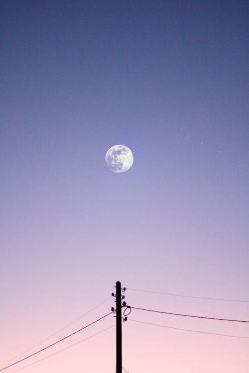 Free Full moon rising in a pastel sky with silhouetted utility pole, creating a serene dusk atmosphere. Stock Photo