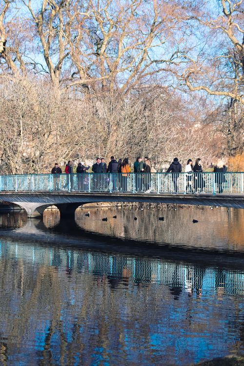 Free Visitors enjoying a fall day on a scenic bridge in a London park, reflecting on the water below. Stock Photo