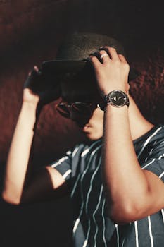 一位时尚的年轻人在户外戴着时尚的手表和帽子摆姿势，展现现代时尚造型