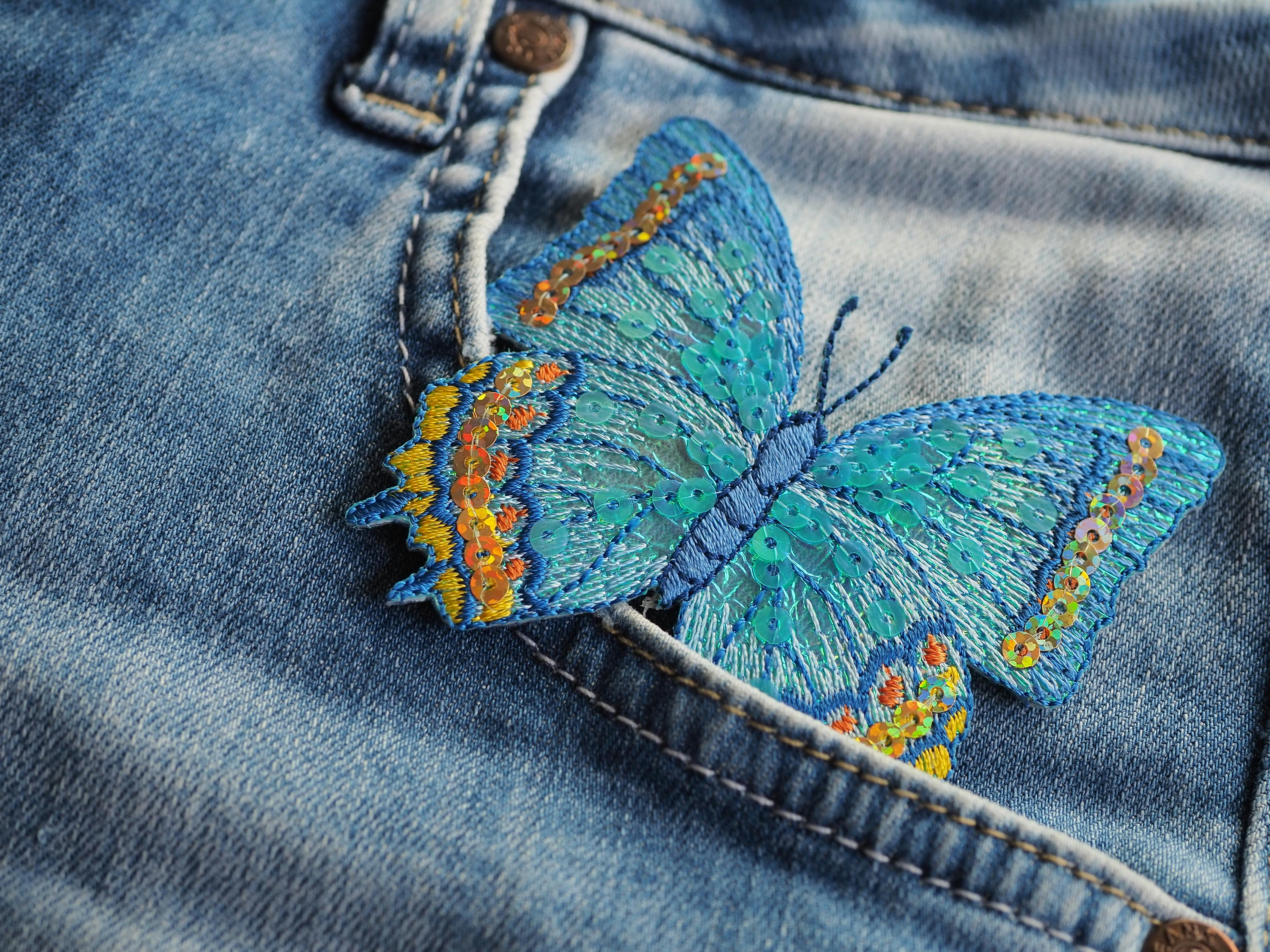 A blue butterfly embroidered into the pocket of a pair of jeans