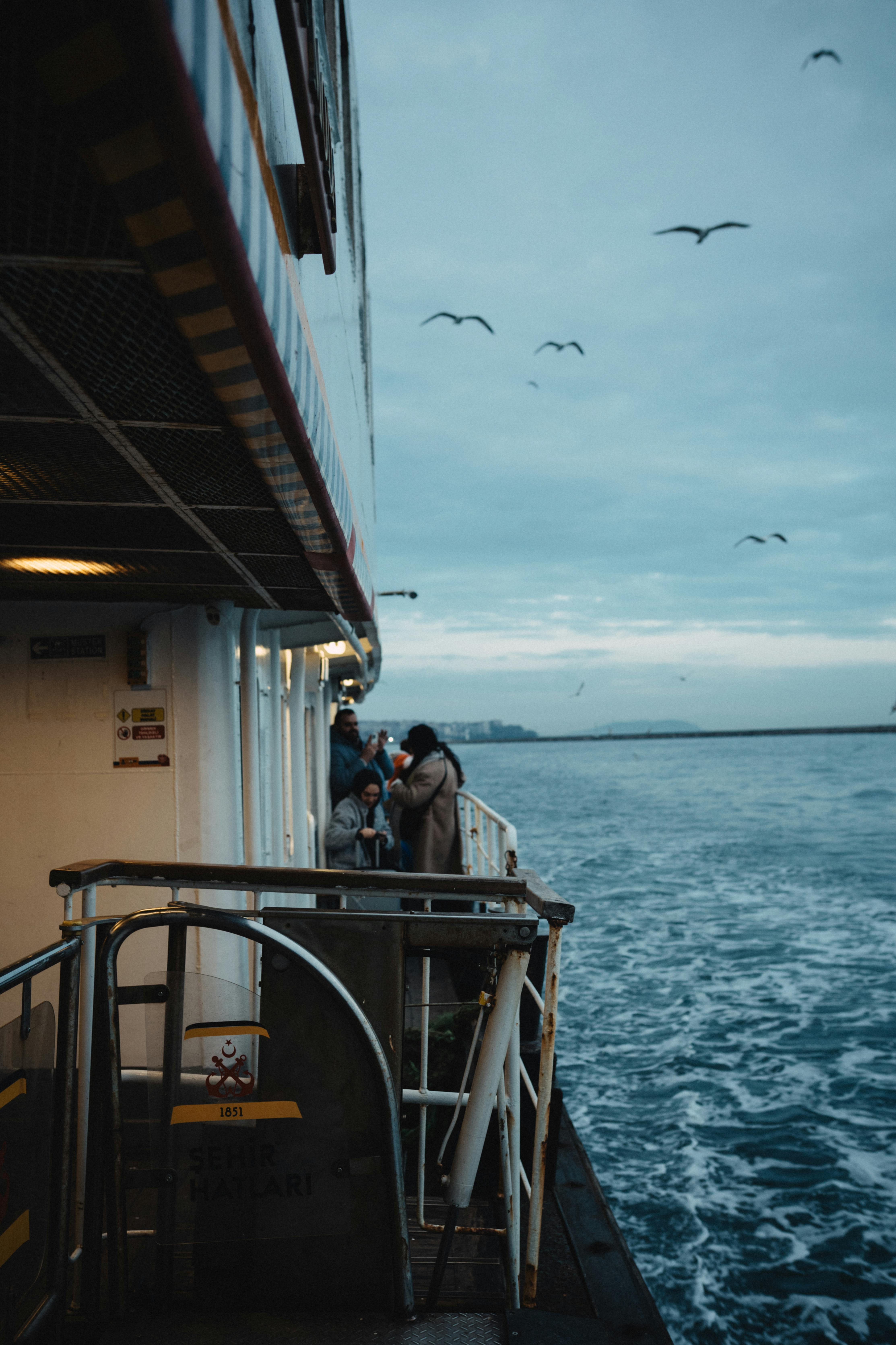 Free Passengers enjoy a peaceful ferry ride as seabirds fly over the calm ocean waters at twilight. Stock Photo