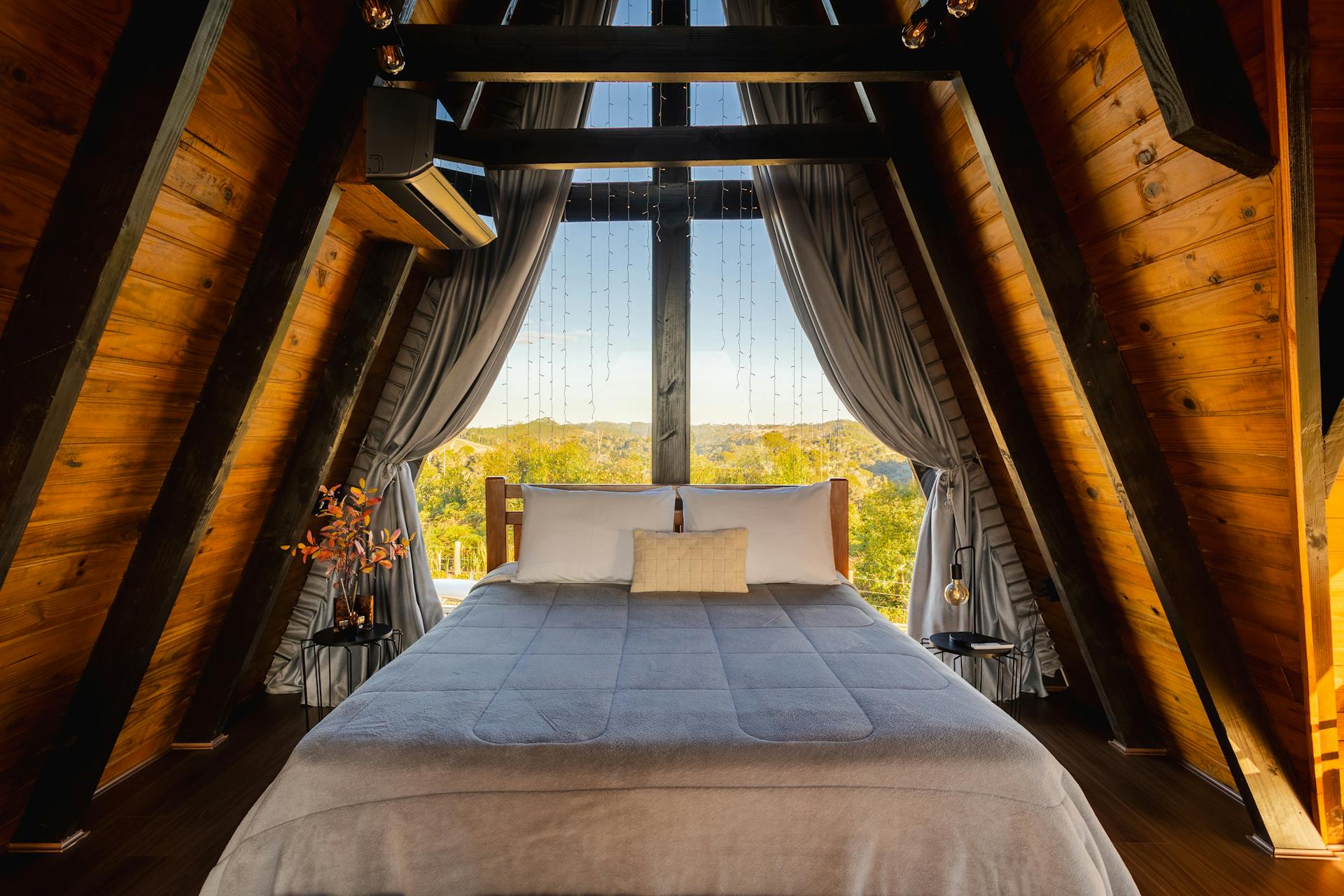 A cozy A-frame cabin bedroom with a rustic wooden interior and scenic outdoor view.