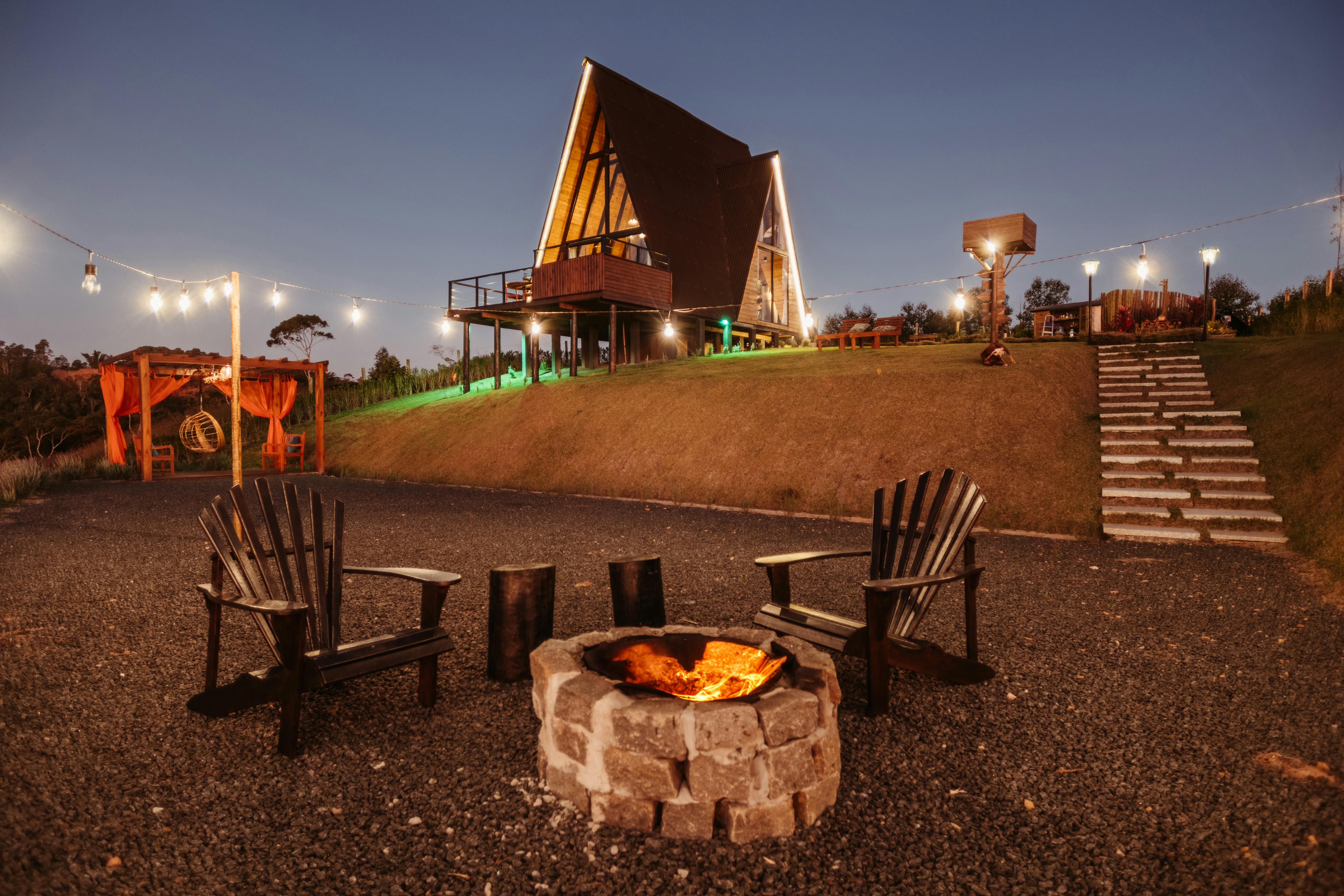 A serene evening at a firepit with an illuminated A-frame cabin in the background, perfect for leisure.