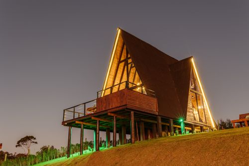 Free A modern A-frame cabin with warm lighting on a grassy slope during twilight. Stock Photo