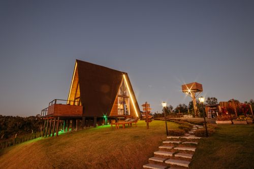 Free A cozy A-frame cabin with warm lights nestled on a grassy slope, perfect for a serene evening getaway. Stock Photo