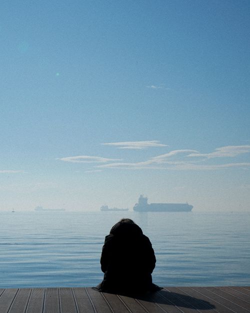 Free Person sitting on a dock in Thessaloniki, Greece, overlooking a calm sea with ships. Stock Photo