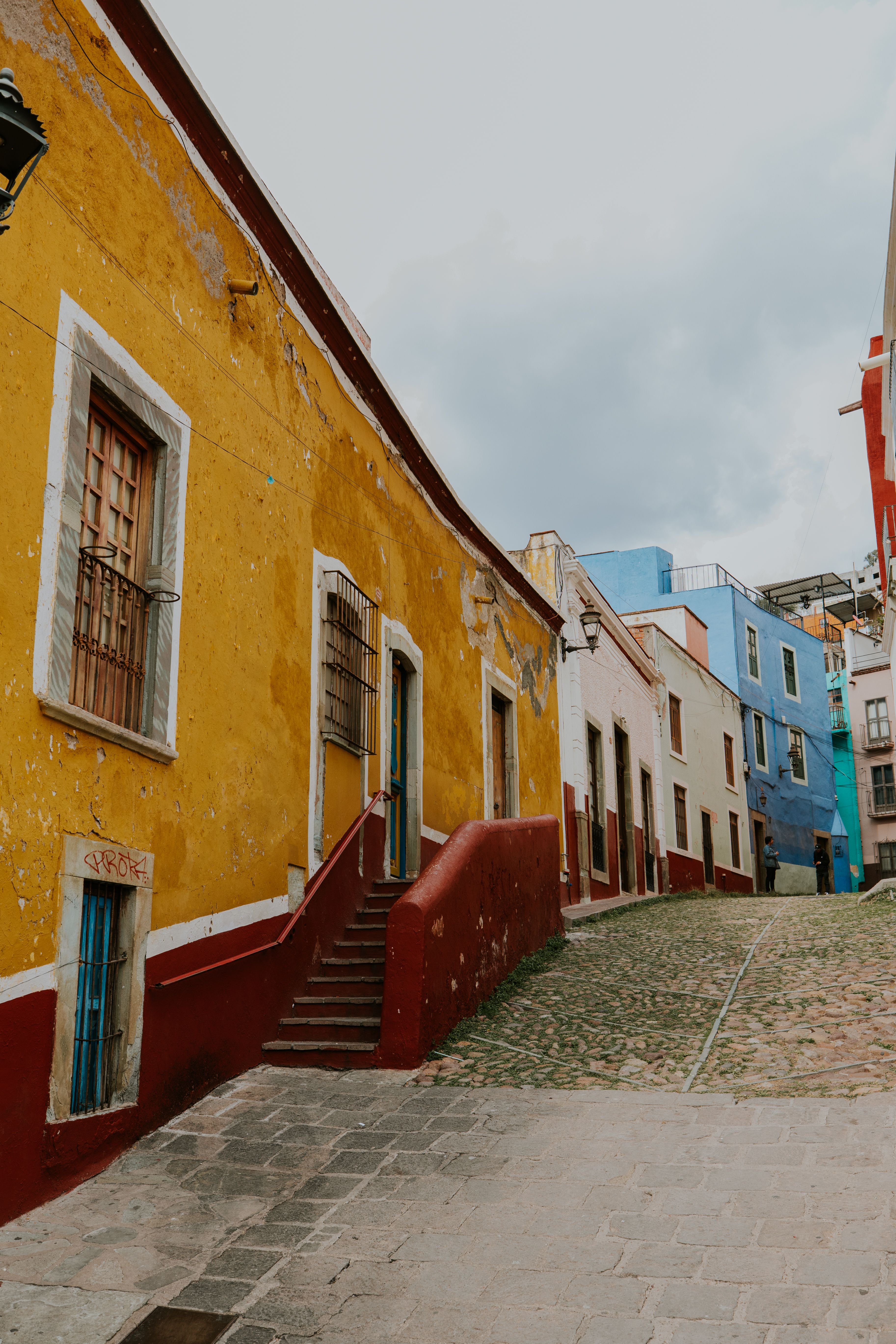 Fotomural Casas vibrantes bordean una calle de piedras en Guanajuato, México, mostrando fachadas coloridas.