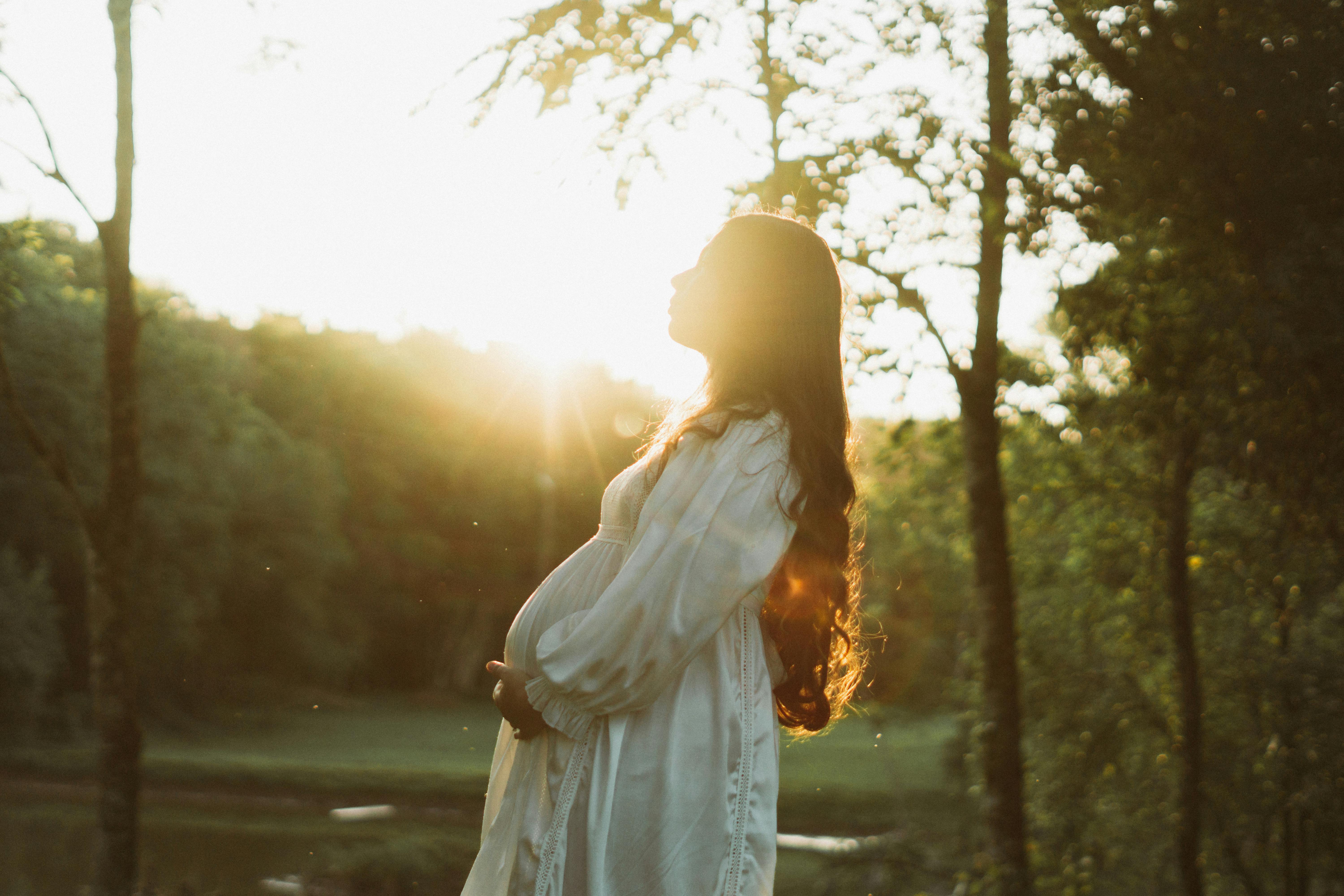 pregnant woman in a dress standing outside and touching her stomach