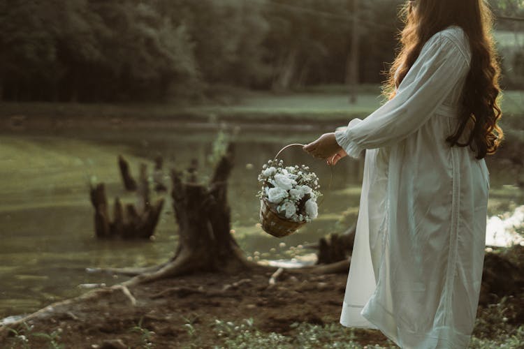 Pregnant Woman Holding A Basket With White Flowers And Standing Outside 