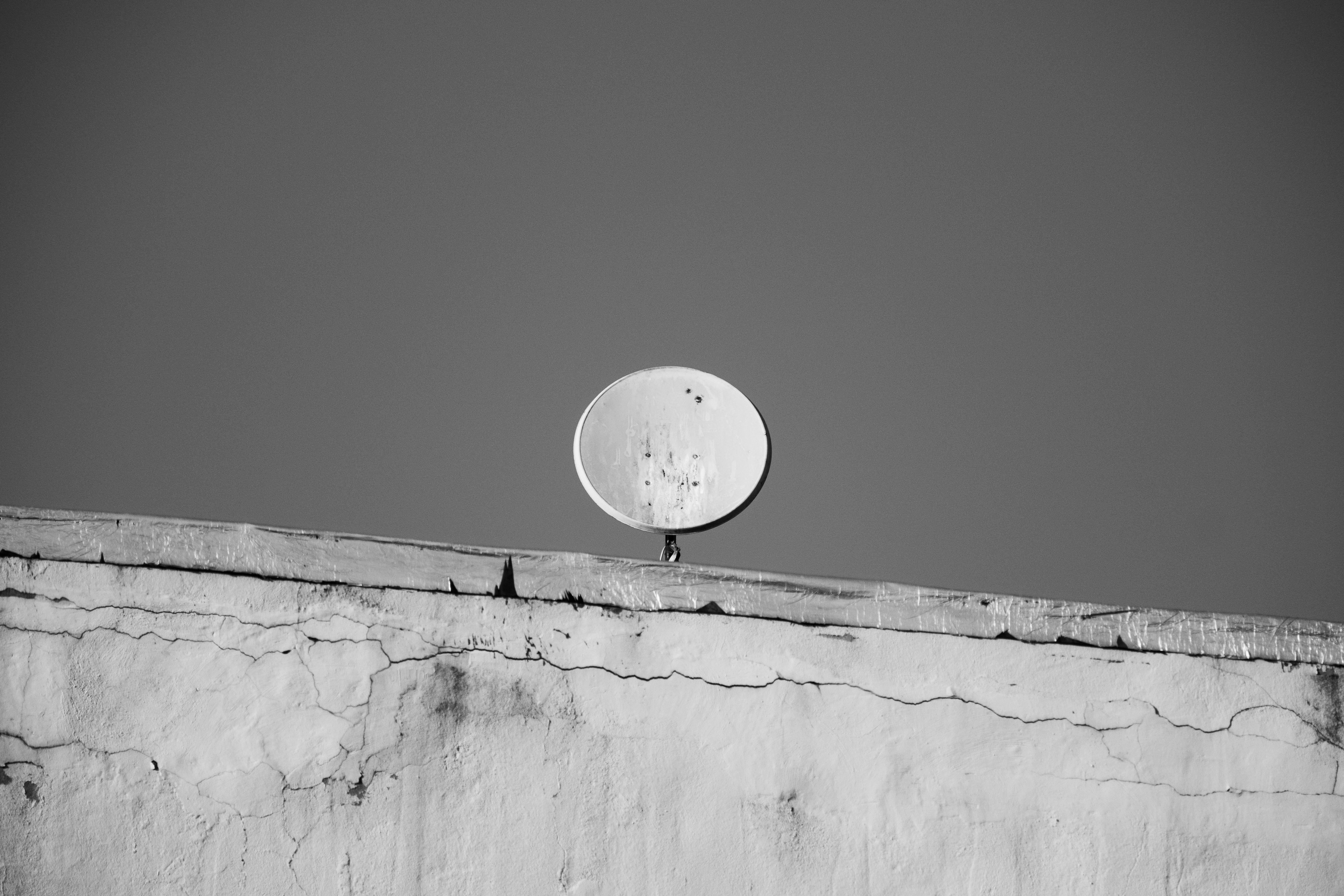 Monochrome photo of a satellite dish on a building rooftop against the sky.