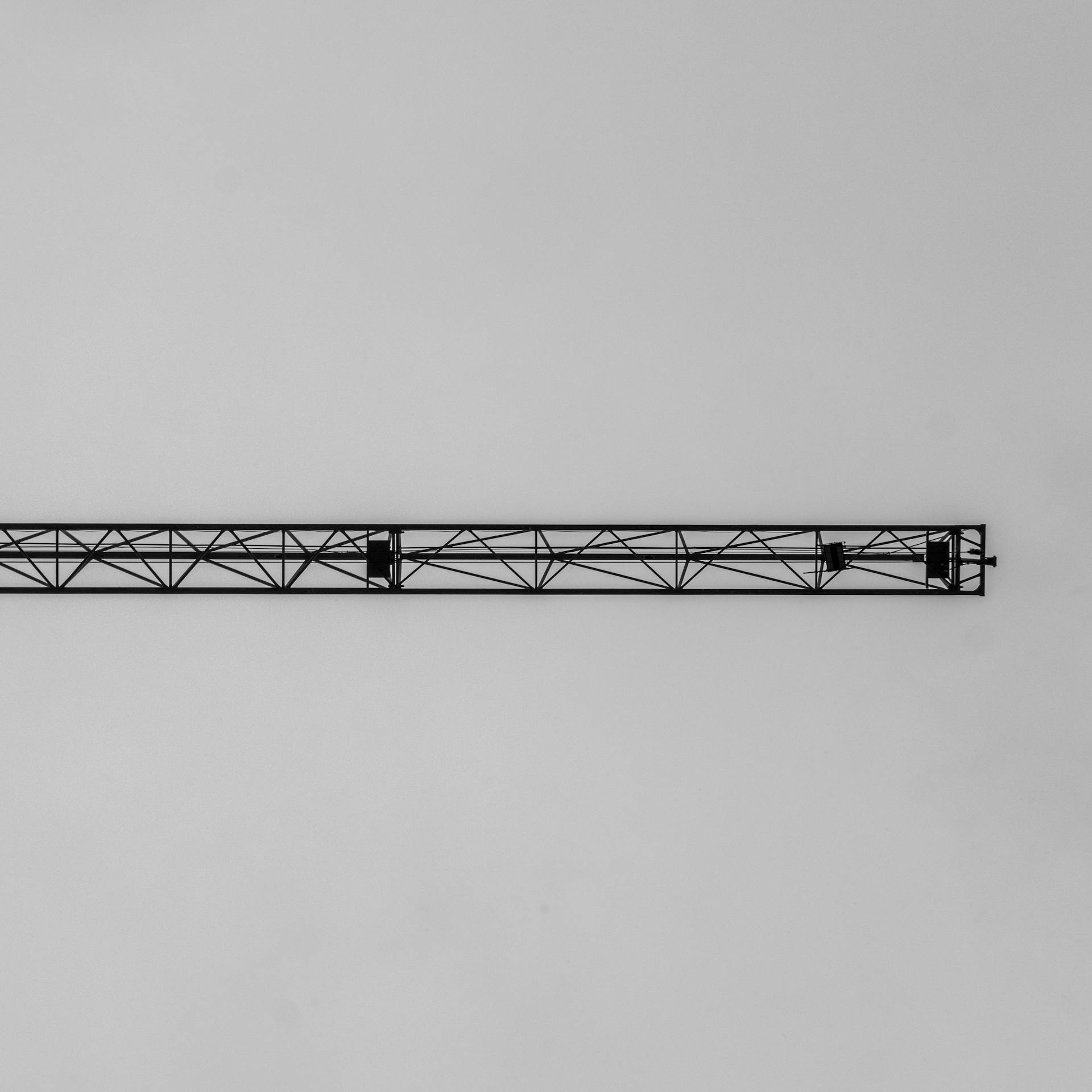 Minimalist photo of a crane arm against a neutral grey sky, showcasing industrial simplicity.